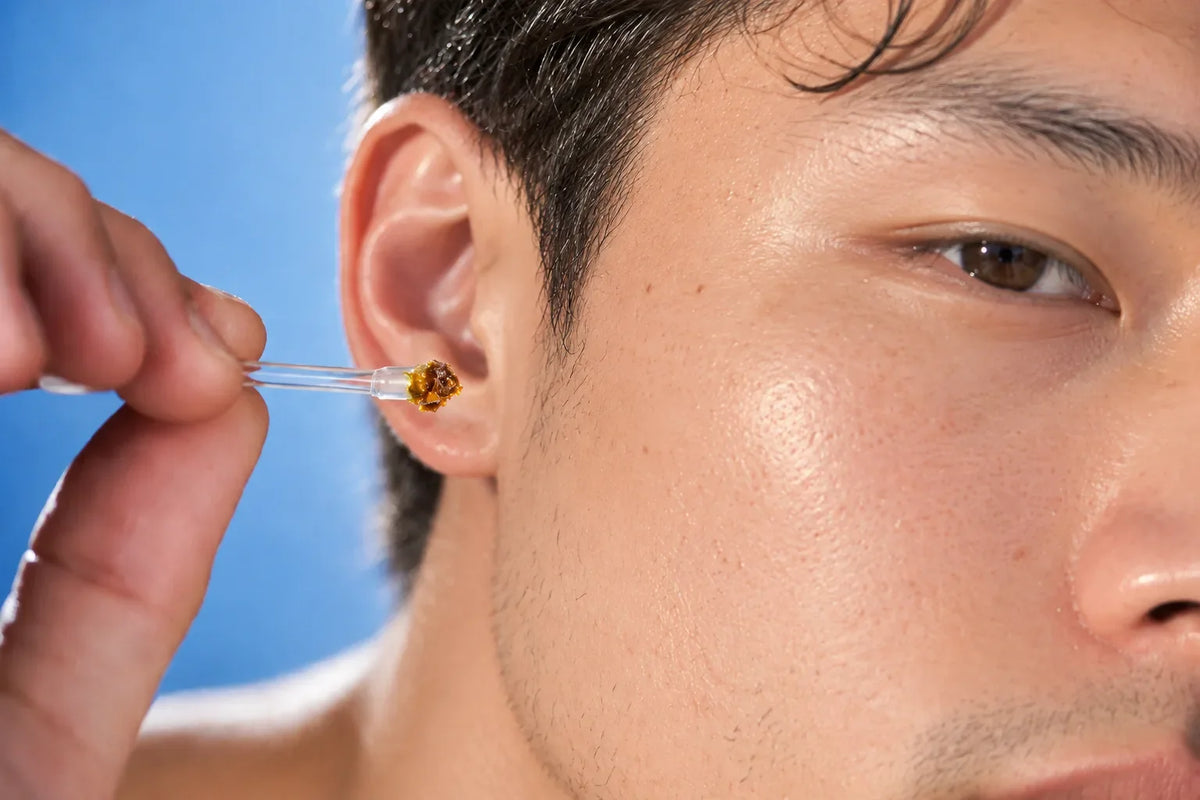 Close-up of a man's ear with a clear ear cleaning stick held at the outer ear