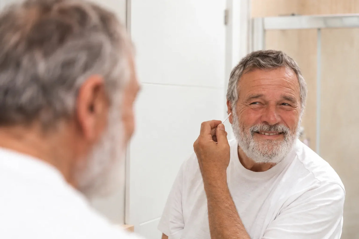 Smiling older man looking in a bathroom mirror while touching the outer edge of his ear